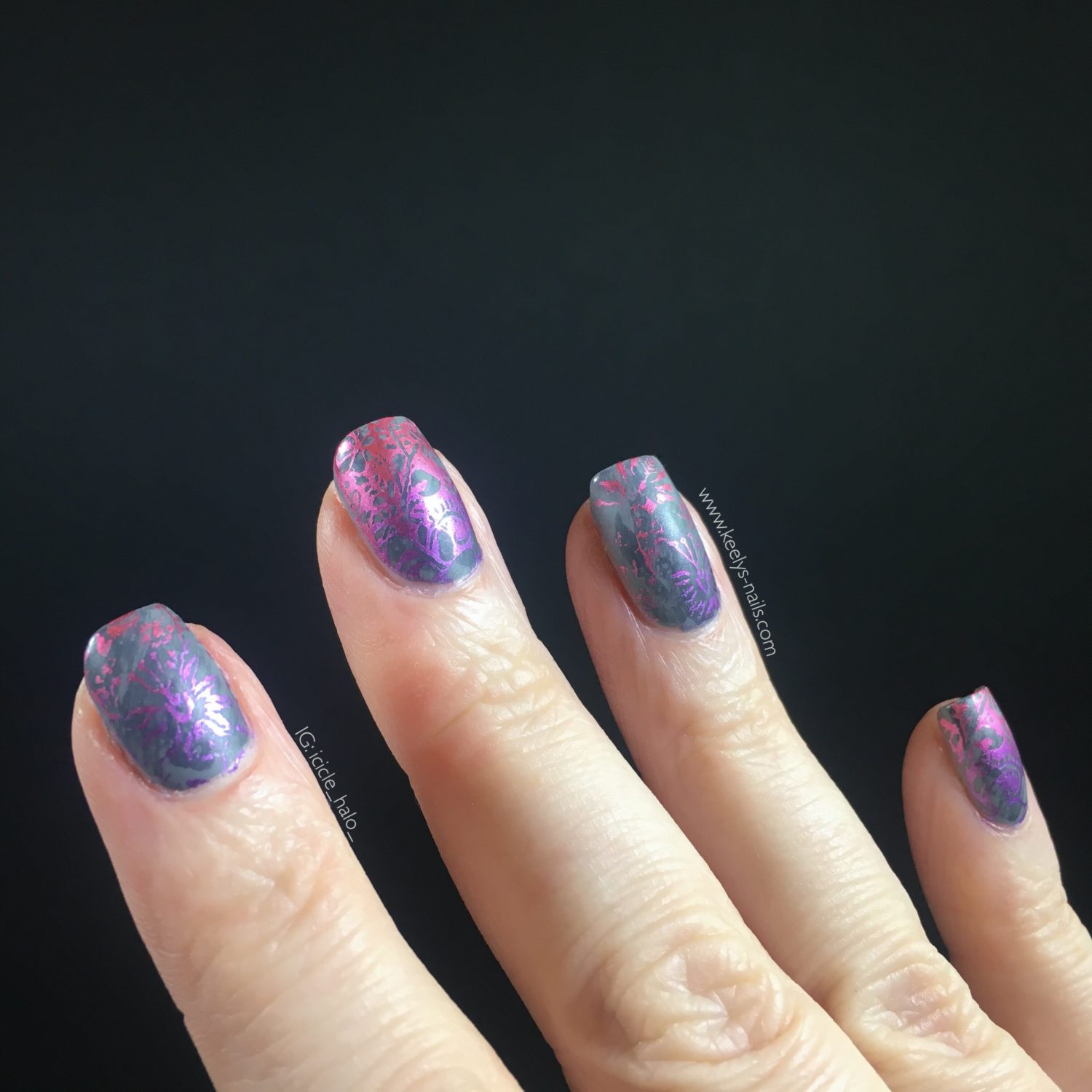 Right hand fingers on a black background with grey matte nails with a pink and purple gradient stamping design