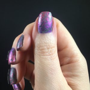 Right hand thumb with fingers curled over behind, grey nail art with pink and purple stamping