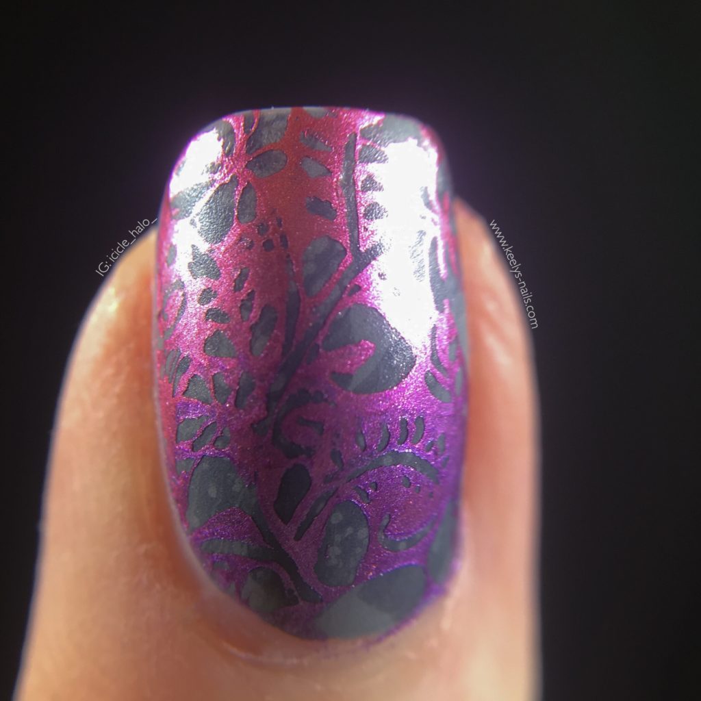 Macro of right middle fingernail with shiny metallic stamping in pink and purple, with a matte grey background behind the stamping
